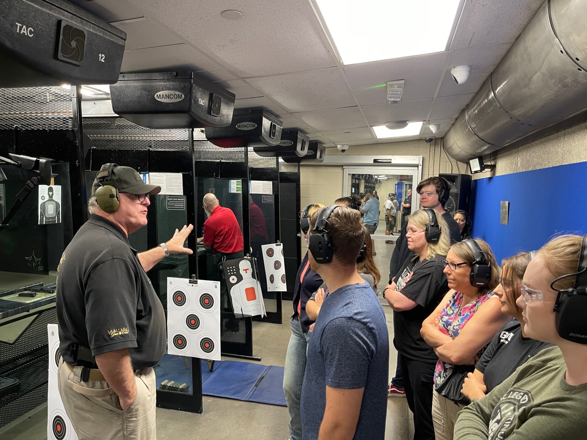 An instructor giving a safety briefing to a group of students wearing hearing protection inside an indoor shooting range