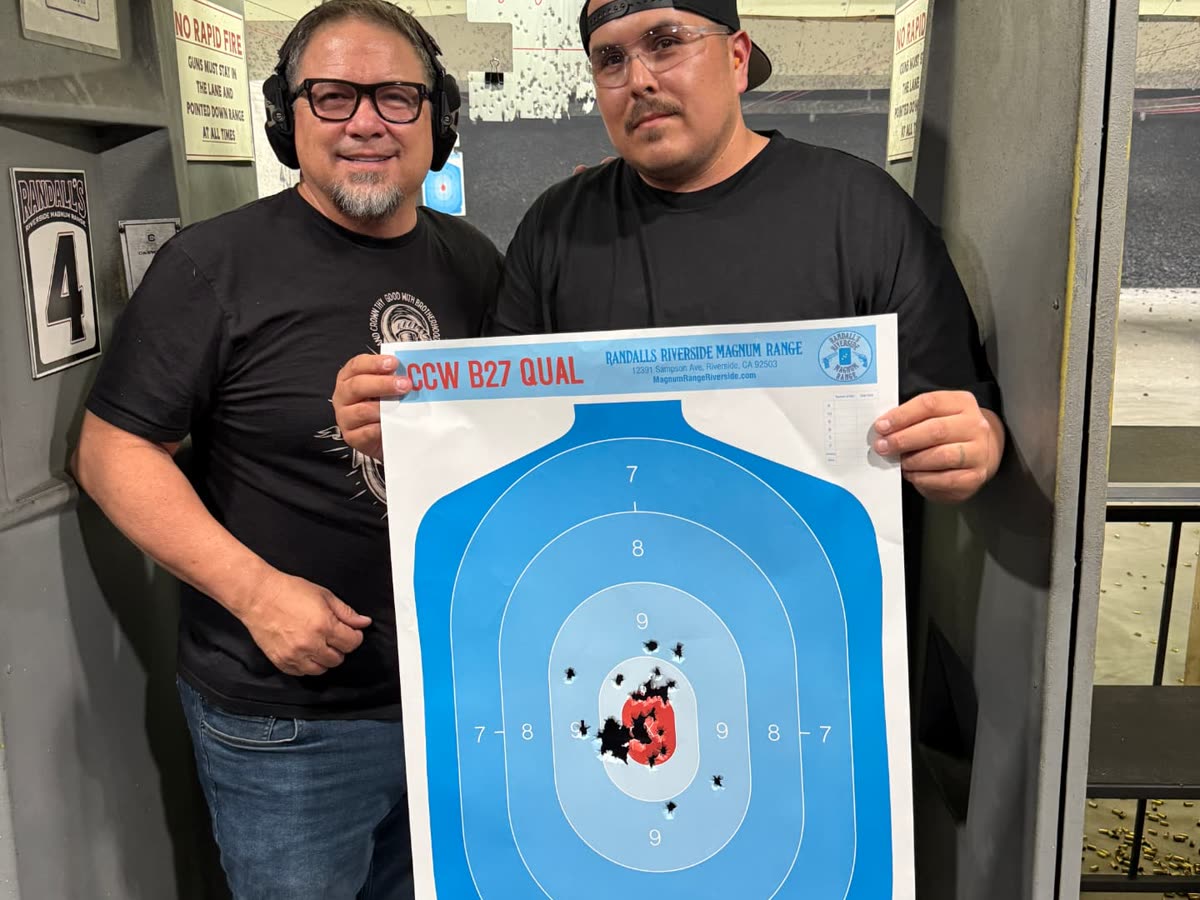 An instructor and a student standing in an indoor range lane holding a completed CCW B27 qualification target